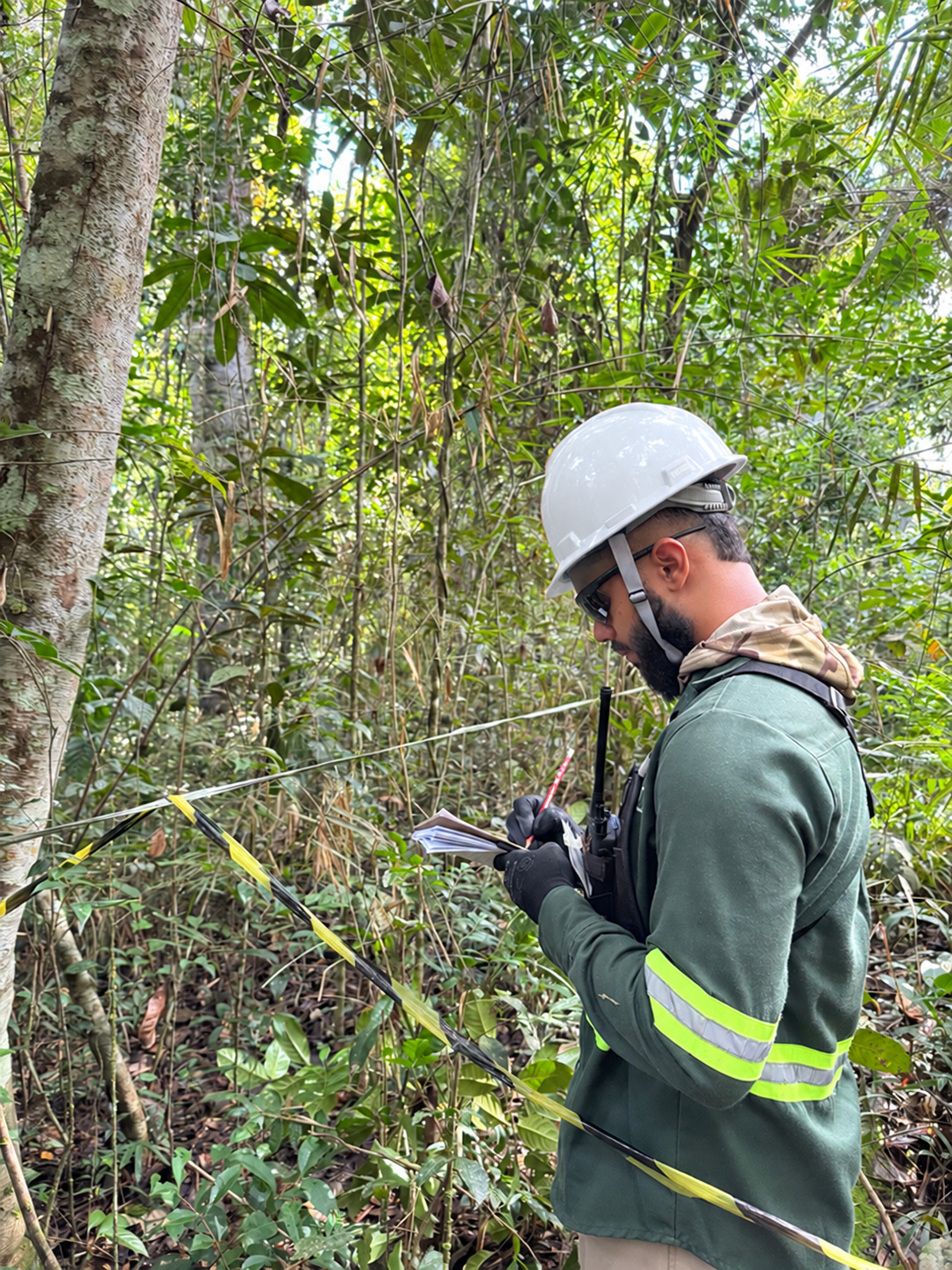 Profissional em atividade de campo em área de vegetação, realizando registro técnico.
